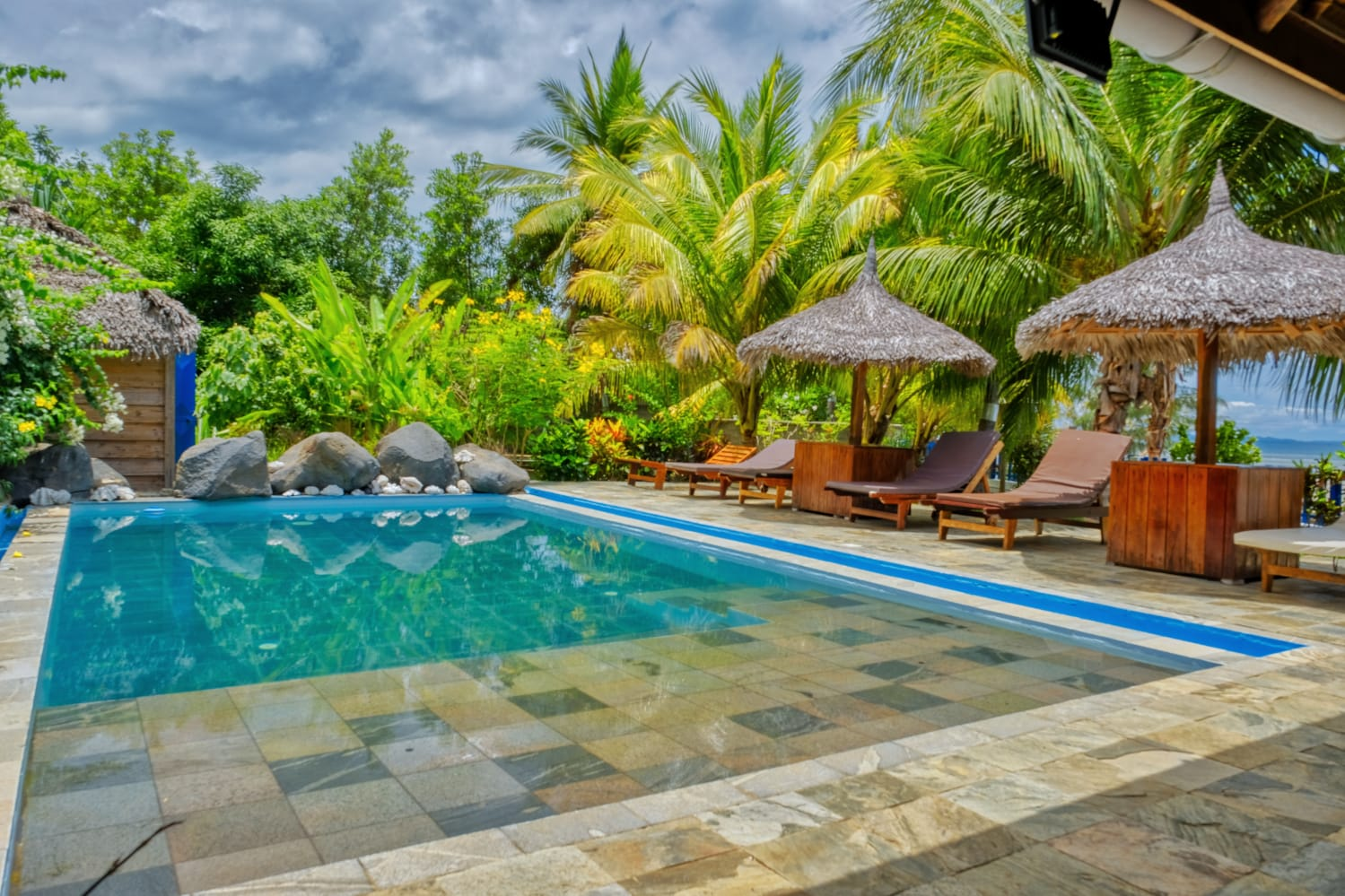 Piscine, transats et parasols en paillote d’une villa à Nosy Be